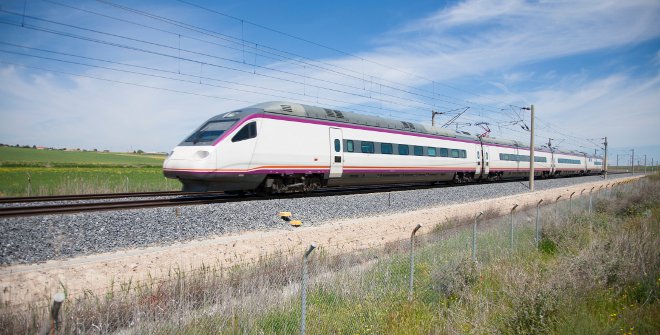 Tren de alta velocidad AVE desplazándose sobre vías al aire libre en un paisaje rural con cielo despejado.